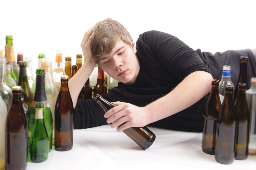 young adult male laying on the ground holding a beer bottle surrounded by empty beer bottles